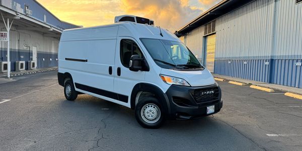 White refrigerated delivery van parked outside warehouse at sunset.