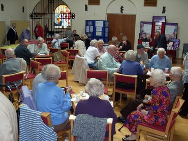 a room full of older people sitting on chairs arranged in groups, having conversations