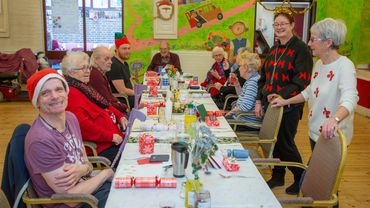 a group of people of different ages sit and stand near a table waiting to eat Christmas dinner