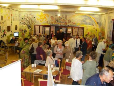 a colourful room is filled with a crowd of older people chatting in small groups