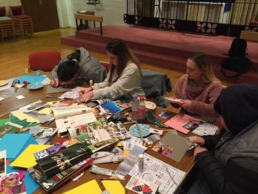 young women sit at a table making collages from magazine pages