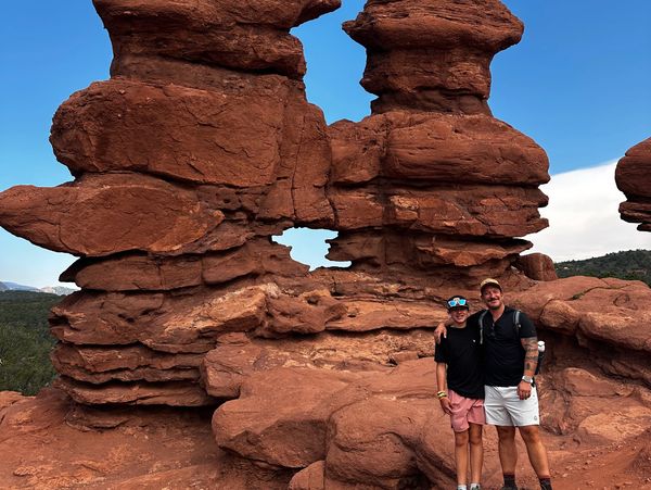 Two people posing in front of unique red rock formations under a clear blue sky.