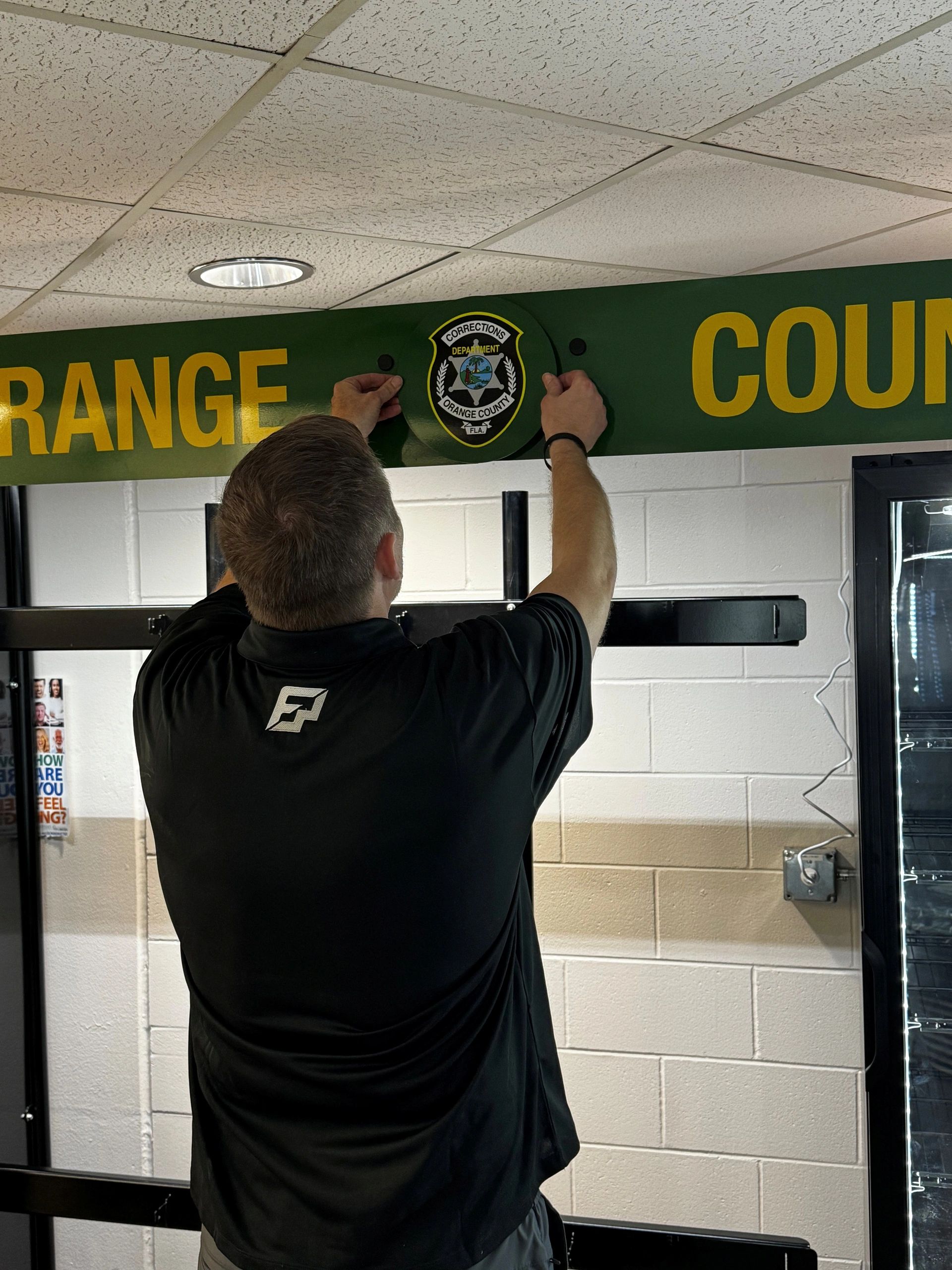 Man putting up Orange County Corrections emblem.