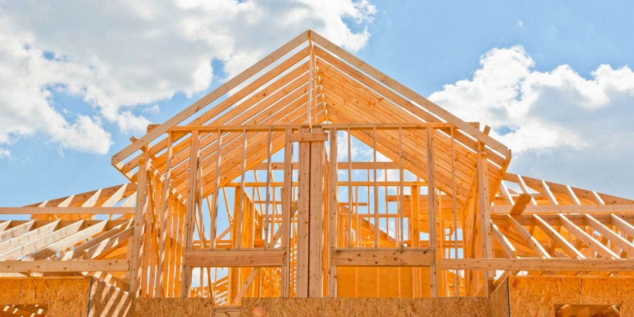 Wooden house frame under construction against a blue sky.