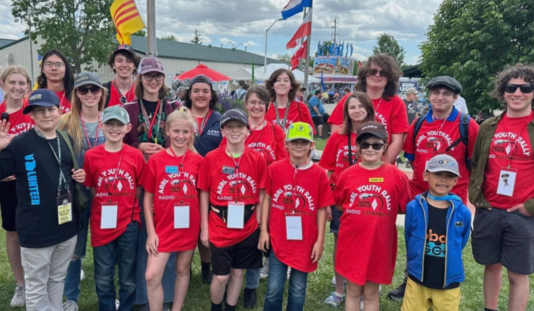 Group of smiling youth wearing red ARRL Youth Rally shirts outdoors.
