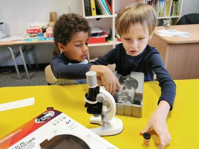 Two young boys exploring a microscope set on a yellow table.