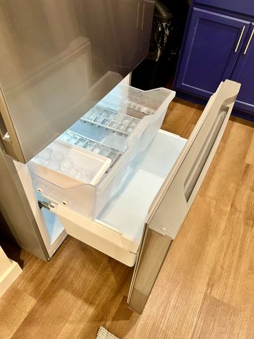 Open freezer drawer with ice trays inside a modern kitchen.