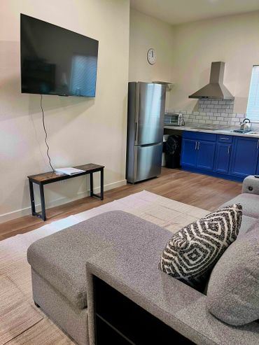 Modern living room with gray sofa and kitchen area with blue cabinets.