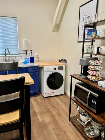 Compact kitchen corner with washer, coffee station, and microwave on wooden shelves.