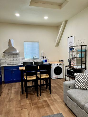 Modern kitchen with blue cabinets, wooden chairs, and a cozy living area.