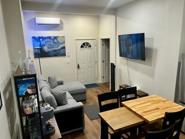 Cozy modern living room with gray sofa, wooden dining table, and wall-mounted TV.