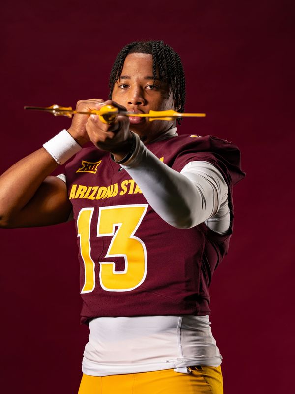 Arizona State football player aiming a bow with intense focus.