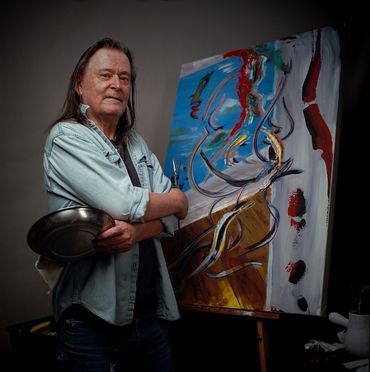 An artist posing confidently beside his abstract painting in a studio.