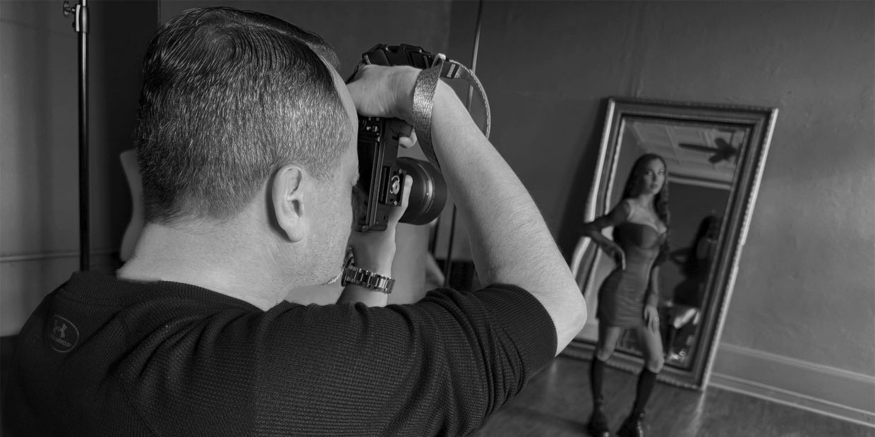 Photographer capturing a woman posing in front of a mirror in a studio.