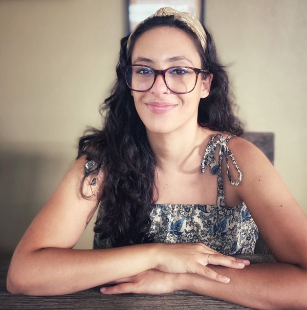 a portrait of the writer wearing a jute headband, oversized glasses and a summer top.