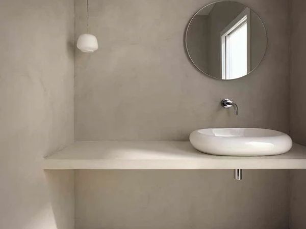 Minimalist bathroom with a round mirror, hanging light, and a sleek white sink on a floating counter.