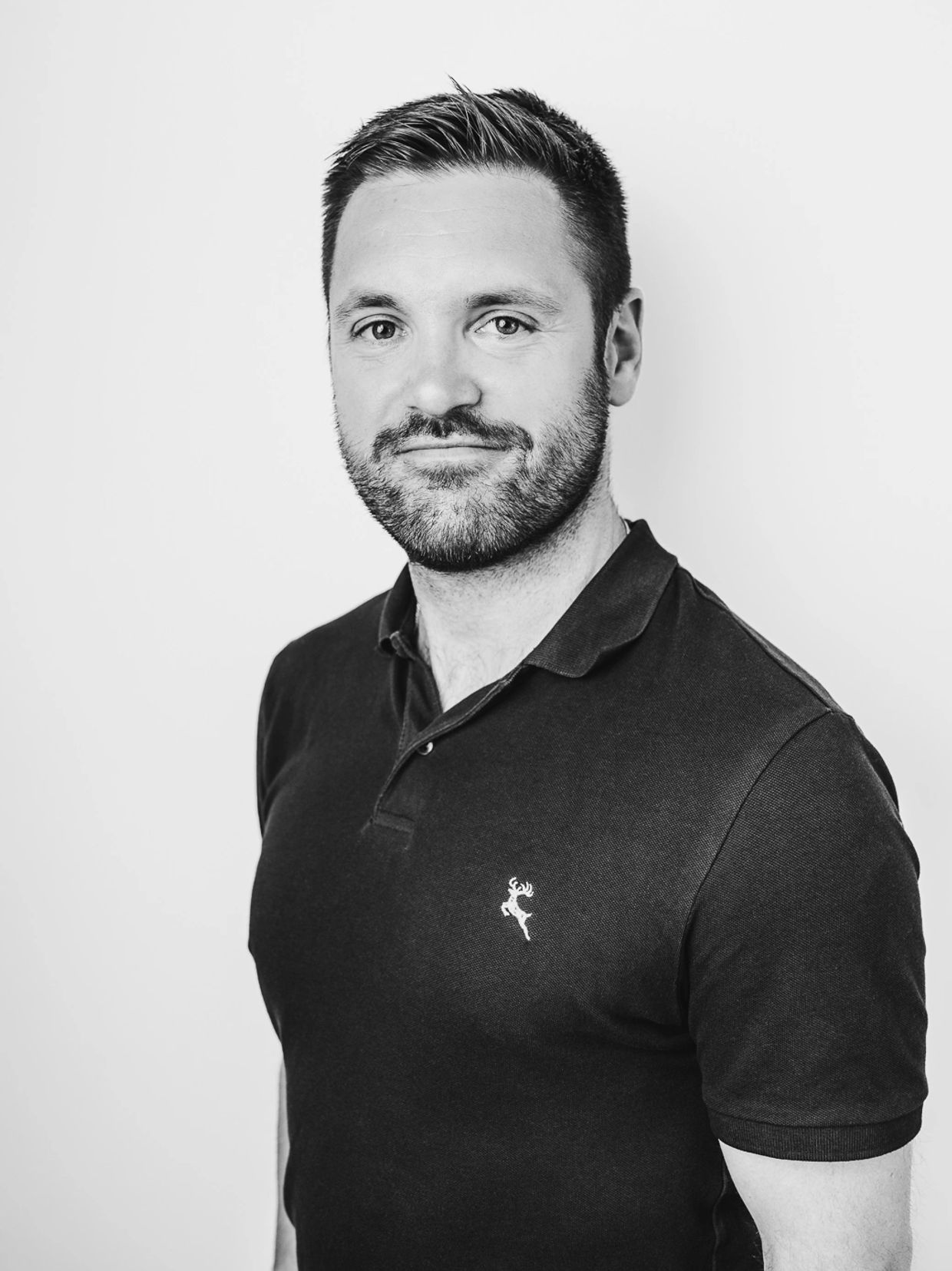 Black and white portrait of a man with a trimmed beard wearing a polo shirt.