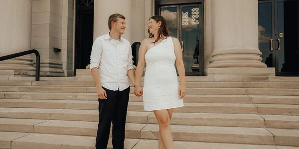 A man and woman holding hands while standing on steps for wedding photos. 
