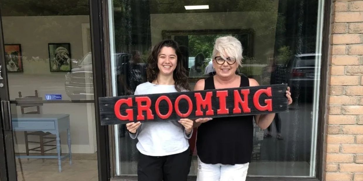 Ellice and Shauntra are holding a sign that says grooming in front of their new grooming salon