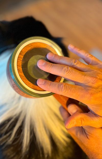 Hand playing a wooden drum with fur details.