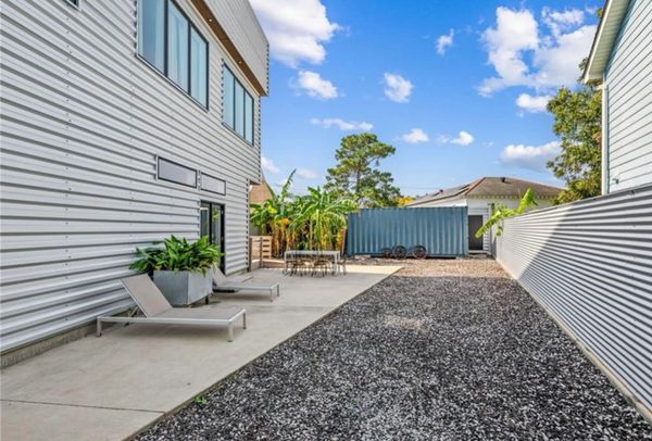 Modern outdoor patio with lounge chairs and a gravel yard under a blue sky.