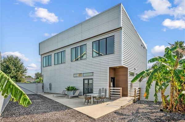 Modern metal-clad house with outdoor seating and tropical plants.
