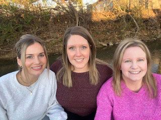 Three women sitting outdoors, smiling.