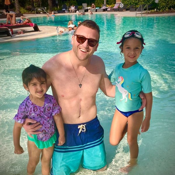 Man with two girls smiling in a swimming pool on a sunny day.