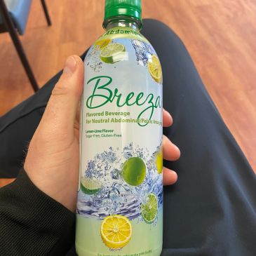 Hand holding a bottle of Breeza lime-flavored beverage for neutral abdominal pH.