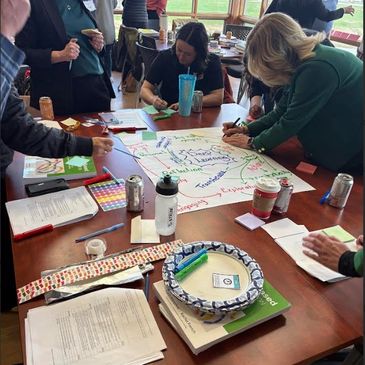 People collaborating around a table filled with papers and drinks.