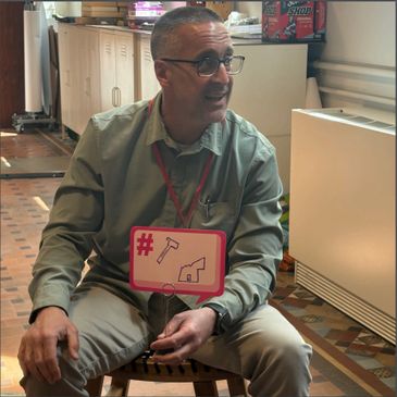 Man sitting indoors holding a sign with tools icons.