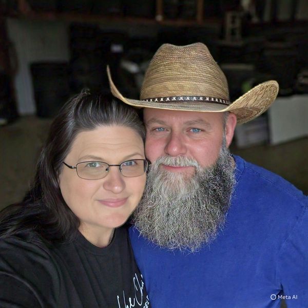 Couple posing closely, man with a beard and cowboy hat, woman with glasses.