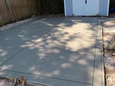 Newly poured smooth concrete slab in backyard near a shed.