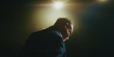 Man in a suit spotlighted from above in dramatic lighting.
