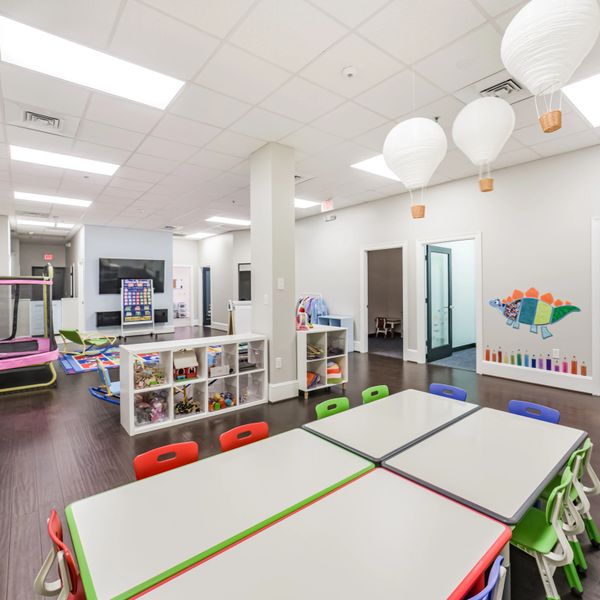 Bright, colorful daycare classroom with tables, chairs, and playful decorations.