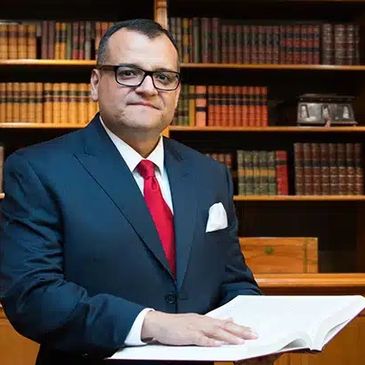 Man in suit and red tie reading a book in a library.