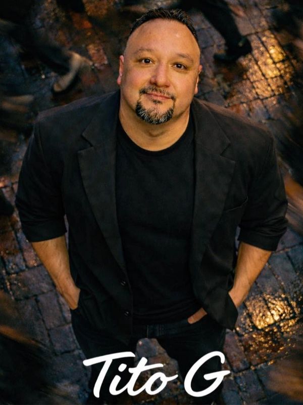 Man in black jacket looking up, surrounded by blurred motion on wet cobblestone.