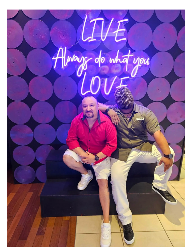 Two men posing in front of a neon sign that says "Live Always do what you Love."