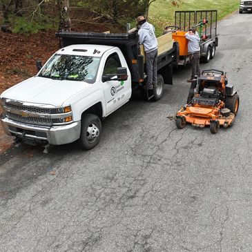 Two workers prepare equipment next to a white truck and trailer on a cracked road.