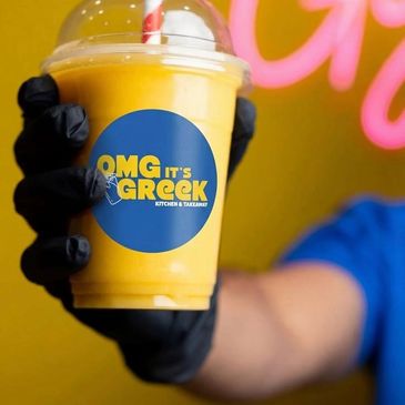 Hand holding a mango smoothie with Greek restaurant branding.