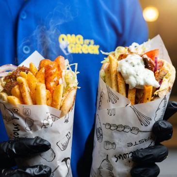 Two greasy, delicious gyro wraps held by a person in black gloves.