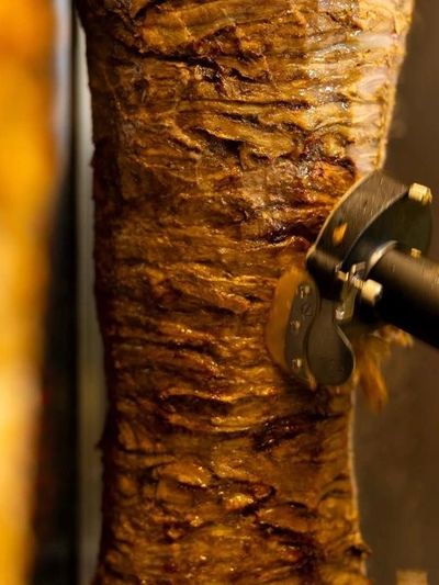 Close-up of meat rotating on a vertical rotisserie being sliced.