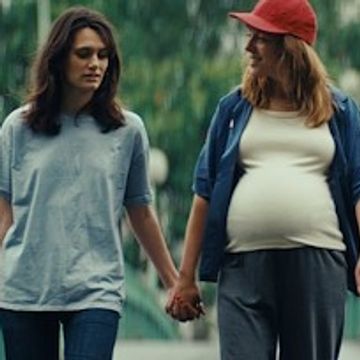 Two women holding hands, one visibly pregnant, walking outdoors.