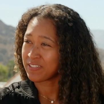 Woman with curly hair outdoors, wearing a black jacket.