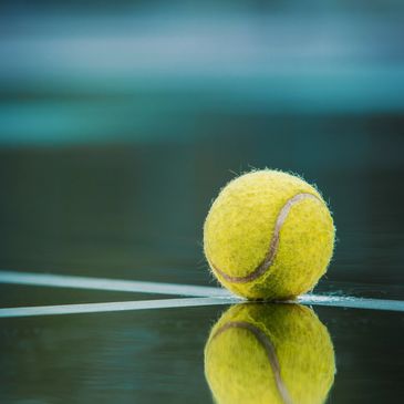 Tennis ball on wet court reflecting on surface.