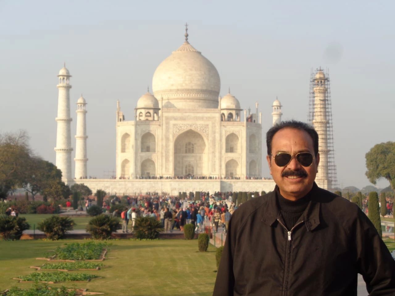 Man posing in front of the Taj Mahal on a sunny day.