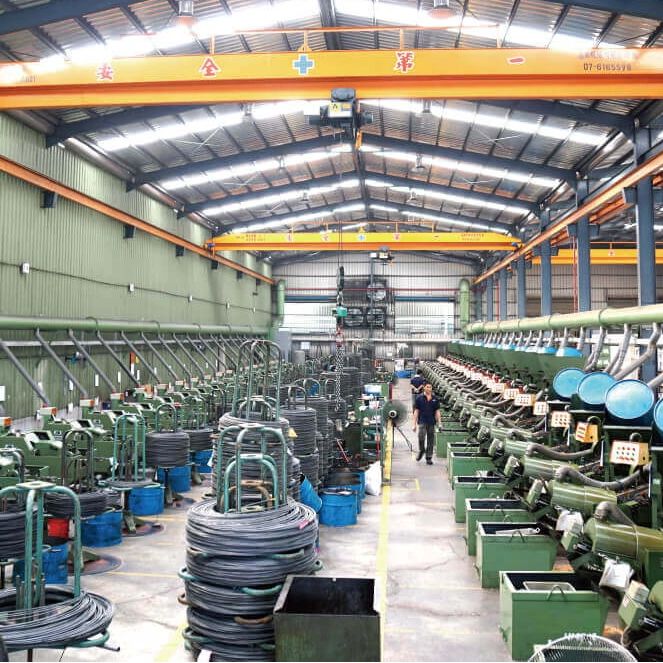 Interior view of a large factory with machinery and coils of wire.