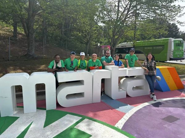 Group posing with large 'marta' letters outdoors near a bus.