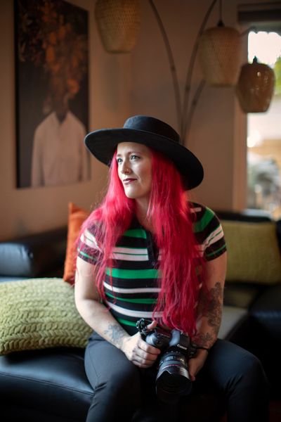 Photographer with red hair and a hat holding a camera in her lap as she is looking toward a window