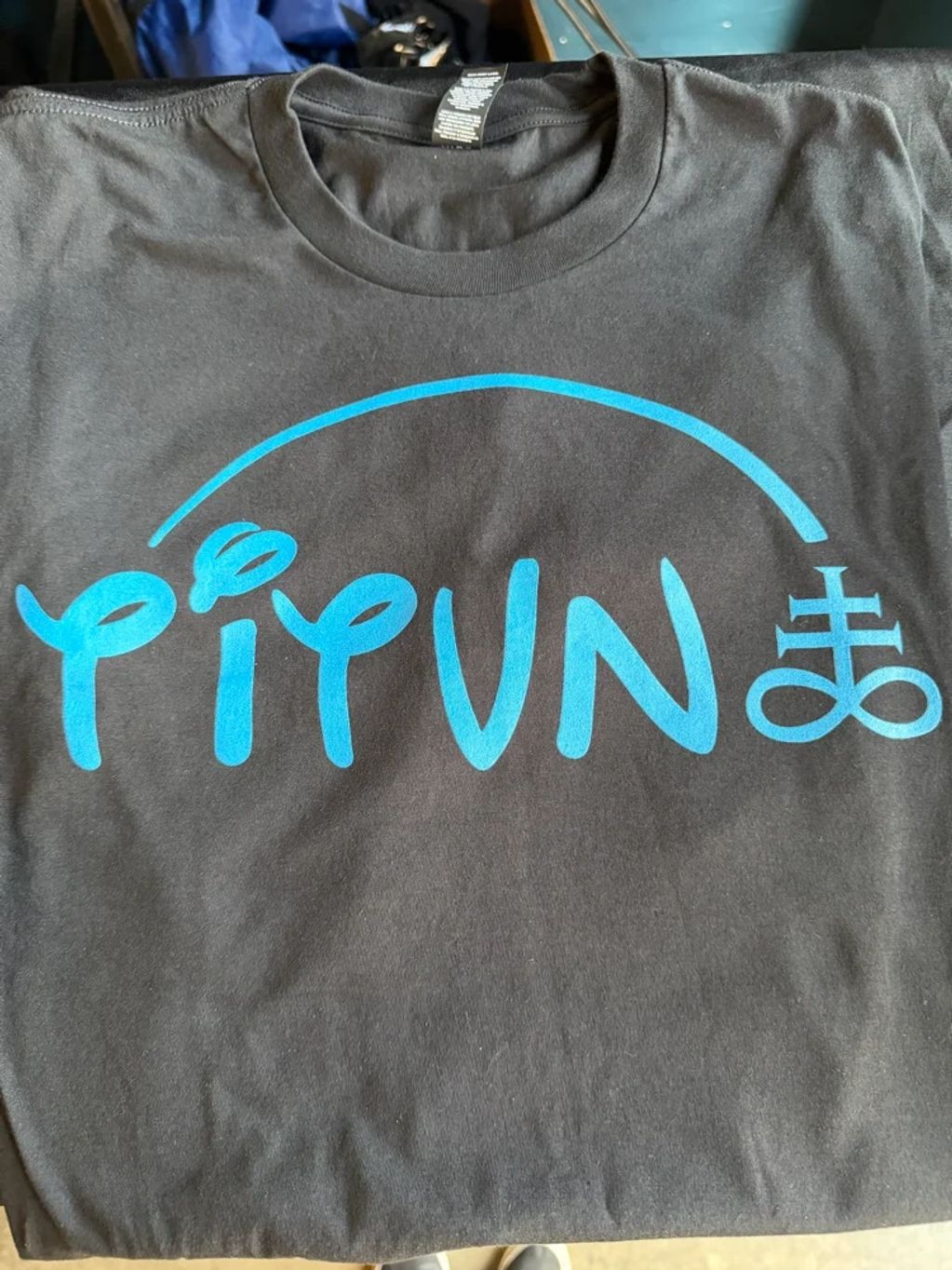 Black t-shirt with blue stylized text and symbols on front.